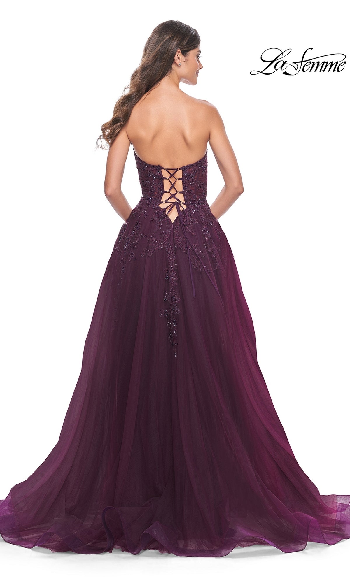 A woman faces away, wearing the La Femme Lace-Up Long Sweetheart Prom Dress 32304—a strapless deep purple A-line gown with a lace-up back and flowing tulle skirt.